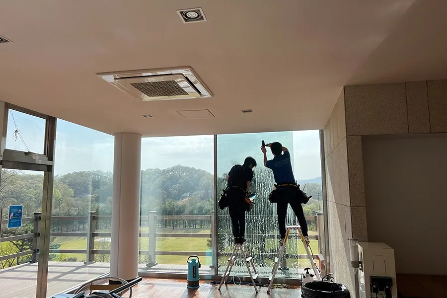 시공 기사가 사다리 없이 그늘집 유리 지붕에 필름을 부착하는 모습